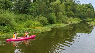 Two people paddling a red canoe along a calm, tree-lined river on a sunny summer's day.