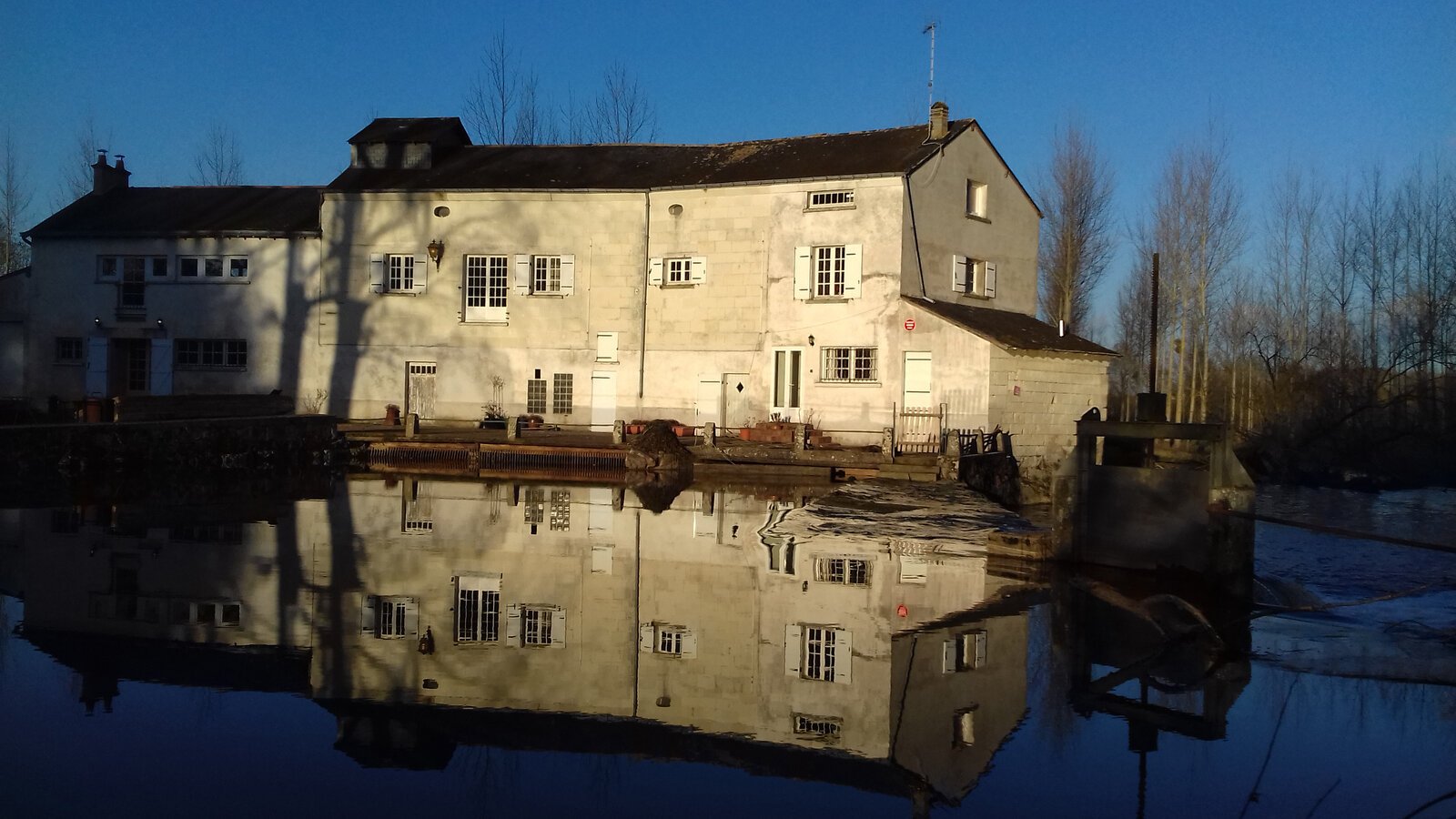 Un grand moulin à eau en pierre claire se reflétant dans une eau paisible par une tranquille journée d'hiver dans la vallée de la Loire, en France.