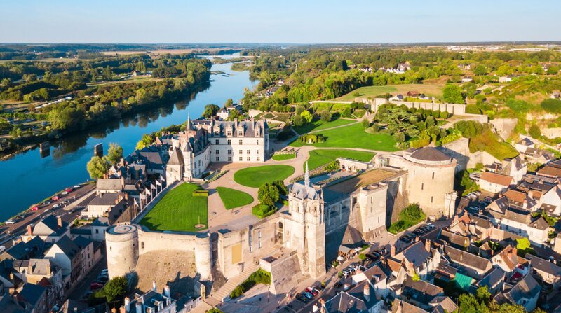An aerial view of the Château d'Amboise and its surrounding historic town, with the wide River Loire curving through lush green landscape beyond.