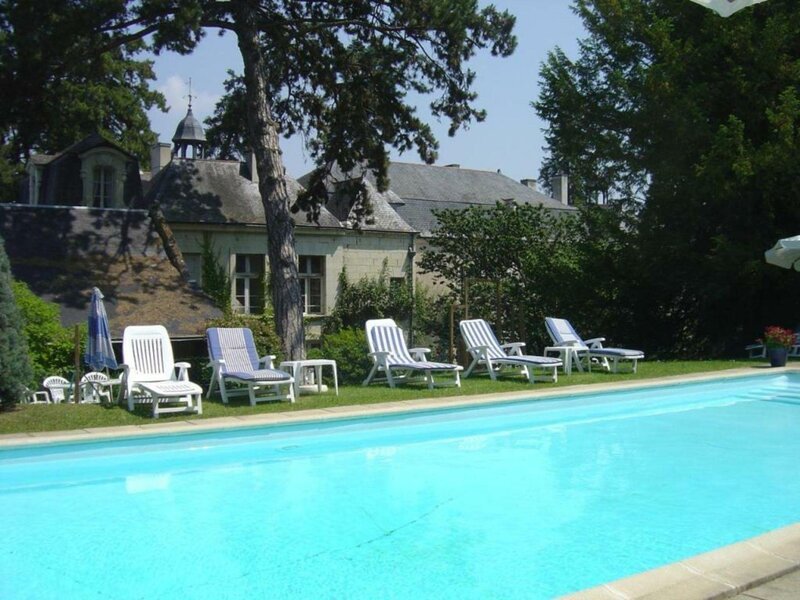 A large outdoor swimming pool with white sun loungers on the terrace, set in front of a traditional French château surrounded by mature trees on a sunny summer's day.