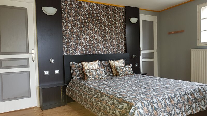 Une chambre double d'hôtel élégamment décorée, avec un mur d'accent à motifs, un couvre-lit assorti, des panneaux peints en gris et un éclairage mural chaleureux.